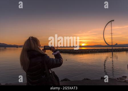 Unerkannte blonde Frau, die ihr Smartphone benutzte, um während des Sonnenuntergangs ein Foto von der Küste zu machen. Stockfoto