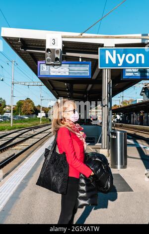 Blonde Frau mit Gesichtsmaske wartet auf ihren Zug im Bahnhof. Stockfoto