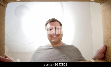 Junger lächelnder Mann, der in das Paket oder den Geschenkkarton schaut Stockfoto