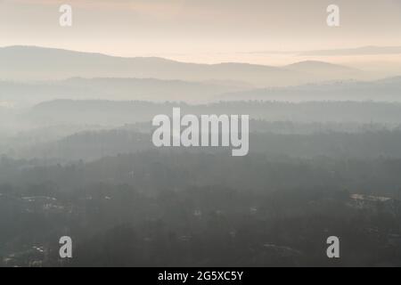 Neblige bewaldete Bergrücken ziehen sich in weichen grau-braunen Schichten unter einem blassen Morgenhimmel in einem weiten Ausblick im Hot Springs National Park, Arkansas, zurück. Stockfoto