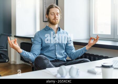 Ruhiger und friedlicher junger Geschäftsmann mit geschlossenen Augen, der im Büro meditiert Stockfoto