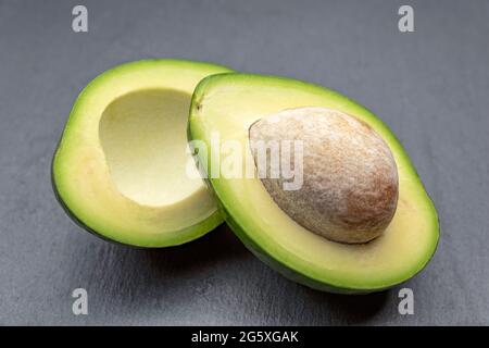 Frische Avocado halbieren. Eine Avocado mit Knochen liegt auf einer schwarzen Steinschale. Gesundes Lebensmittelkonzept. Stockfoto