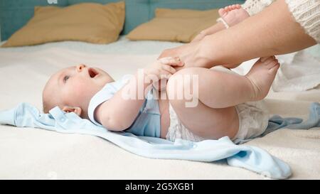 Niedlicher kleiner Junge, der die Mutter ansieht, während sie seine unordentlichen Windeln auf dem Bett wechselt. Konzept der Elternschaft, Babyhygiene und Kinderentwicklung. Stockfoto
