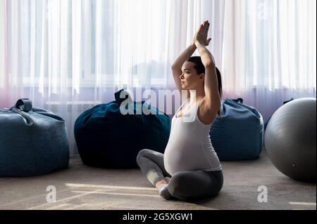 Schwangerin praktiziert Yoga. Eine Frau im dritten Trimester führt Pilates. Kurse zur Vorbereitung auf die Geburt. Warten auf das Baby. Stockfoto