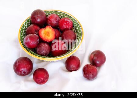 Reife, saftige Pflaumen in einer Schüssel auf weißem Tischtuch-Hintergrund. Stockfoto