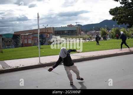 Bogota, Kolumbien. Juni 2021. Ein Demonstrator wirft der kolumbianischen Bereitschaftspolizei (ESMAD) Steine und Debree zu, als die Bewohner von Fontanar - Suba in Bogota, Kolumbien, protestierten und gegen die kolumbianische Bereitschaftspolizei (Escuadron Movil Antidisturbios ESMAD) gegen den Besuch des kolumbianischen Präsidenten Ivan Duque Marquez in einem Park, in dem Bogotas U-Bahn-System gebaut werden soll, zusammenprallten. Inmitten von zwei Monaten regierungsfeindlicher Proteste gegen den Präsidenten Ivan Duque Marquez, Ungleichheiten und Polizeiunruhen während der Proteste am 29. Juni 2021. Kredit: Long Visual Press/Alamy Live Nachrichten Stockfoto