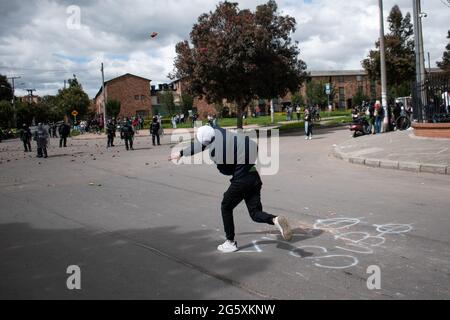 Bogota, Kolumbien. Juni 2021. Ein Demonstrator wirft der kolumbianischen Bereitschaftspolizei (ESMAD) Steine und Debree zu, als die Bewohner von Fontanar - Suba in Bogota, Kolumbien, protestierten und gegen die kolumbianische Bereitschaftspolizei (Escuadron Movil Antidisturbios ESMAD) gegen den Besuch des kolumbianischen Präsidenten Ivan Duque Marquez in einem Park, in dem Bogotas U-Bahn-System gebaut werden soll, zusammenprallten. Inmitten von zwei Monaten regierungsfeindlicher Proteste gegen den Präsidenten Ivan Duque Marquez, Ungleichheiten und Polizeiunruhen während der Proteste am 29. Juni 2021. Kredit: Long Visual Press/Alamy Live Nachrichten Stockfoto