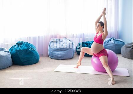Schöne Schwangerin macht Übungen auf einem Fitnessball. Werdende Mutter im letzten Trimester beim Yoga. Stockfoto