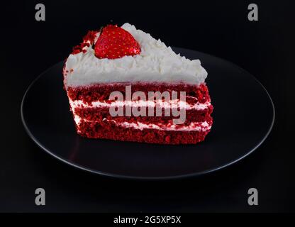 Ein Stück Kuchen mit Proteincreme und Erdbeeren auf einem schwarzen Teller und schwarzem Hintergrund isoliert bedeckt Stockfoto