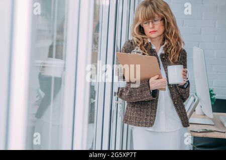 Geschäftsfrau im Büro mit Dokumenten und einer Tasse Kaffee am Fenster Stockfoto