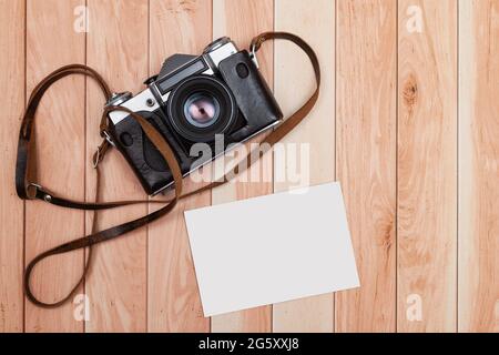 Von oben aus gesehen, befinden sich auf einigen hellen Holzbrettern eine analoge Kamera und ein leeres Foto, das als Modell angepasst werden kann. Stockfoto