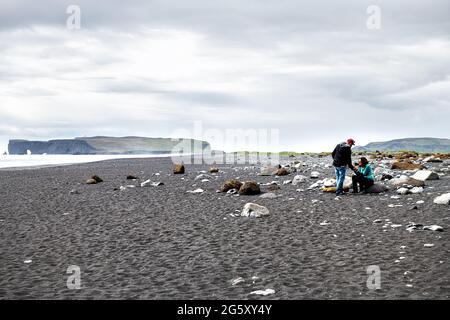 Myrdal, Island - 14. Juni 2018: Reynisfjara schwarzer Sandstrand und Menschen Touristen paaren sich in vulkanischen felsigen Felsformationen mit Küstenlinie in Stockfoto