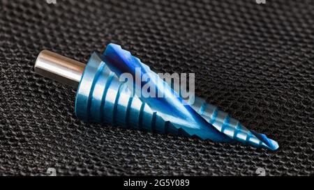 Nahaufnahme des konischen Stufenbohrers mit Spiralnut und blauer Oberfläche auf schwarzem Hintergrund. Ein Nano-beschichtetes Unibit zum Bohren unterschiedlicher Lochgröße. Stockfoto