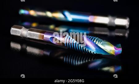 Stahlzapfen und Bohrer in einem Schneidwerkzeug auf glänzendem schwarzem Hintergrund. Schöne Reflektion. Bohr- und Gewindeinstrument im künstlerischen Stillleben. Stockfoto