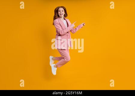 Erfolgreiche Business-Frau in rosa Anzug springen Pinting Zeigefinger an der Seite, isoliert auf gelbem Hintergrund, Shopping. Portrait. Copy Raum für Werbung Stockfoto