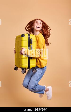 Aufgeregt Reisende Touristen Rotschopf Frau hält Koffer, springen in lässigen Outfit isoliert im Studio. Kaukasische Passagierin, die mit W ins Ausland reist Stockfoto