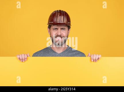 Glücklich reifer Mann Baumeister im Helm hinter gelbem Papier für Kopierraum, Werbung Stockfoto