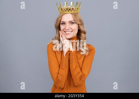 Glückliche blonde Frau in Krone halten Hände. Selbstbewusste Königin. Ausdruck smug. Stockfoto