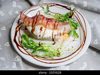 Köstliches leichtes Frühstück pochiertes Ei auf Bruschetta mit Speck, Frisee-Salat und Balsamico-Dressing. Stockfoto