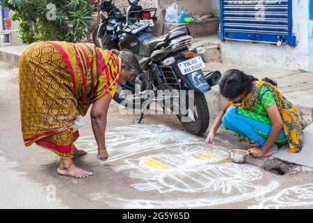 Junge Mädchen und ältere indische Frauen malen einen kolam auf dem Bürgersteig vor ihrem Haus, Trichy, Tamil Nadu, Indien Stockfoto