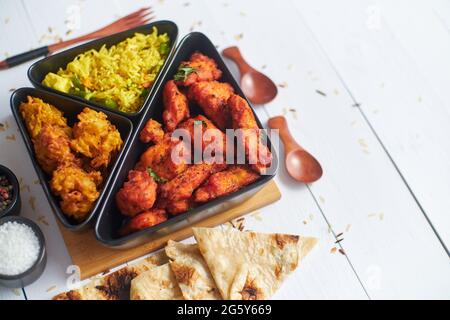 Würziges indisches gebratenes Huhn serviert mit Curry-Gemüsereis, Zwiebel bhajia, Naan-Brot Stockfoto