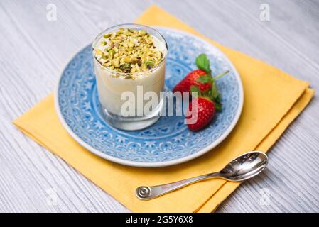 Pistazien-Parfait in einer transparenten Glasschale auf einem blauen Teller mit zwei Erdbeeren, auf einer gelben Serviette mit einem Teelöffel. Stockfoto