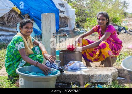 Zwei hübsche junge indische Teenager-Frauen, die am Wasserbrunnen Kleidung waschen, Puducherry (Pondicherry), Tamil Nadu, Indien Stockfoto