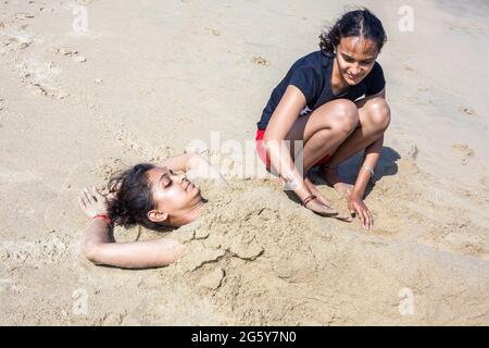 Attraktive indische Weibchen bestattet ihre hübsche Freundin im Sand am Strand, Puducherry (Pondicherry), Tamil Nadu, Indien Stockfoto