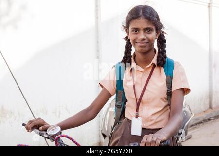 Hübsches indisches Schulmädchen in Uniform mit Rucksack sitzt auf dem Fahrrad und lächelt fröhlich für Foto, Puducherry, Tamil Nadu, Indien Stockfoto