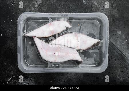 Tiefgefrorene grönländische Heilbutt Steaks Vakuumpaket Set, auf schwarzem dunklen Stein Tischhintergrund, Draufsicht flach liegend Stockfoto