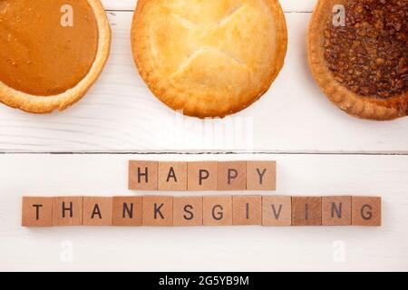 Happy Thanksgiving auf einem weißen Holztisch mit verschiedenen Geschmacksrichtungen von Pies Stockfoto