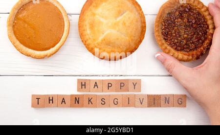 Happy Thanksgiving auf einem weißen Holztisch mit verschiedenen Geschmacksrichtungen von Pies Stockfoto