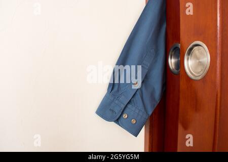 Blaues Hemd aus einem Schrank mit einer Holztür Stockfoto