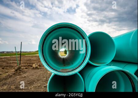 Gestapeltes Wasserhauptrohr mit Glockenanschluss neben einem freiliegenden Graben zur Installation Stockfoto