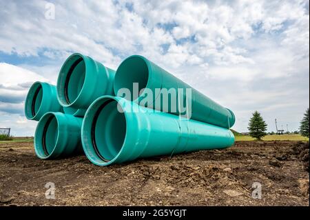 Gestapeltes Wasserhauptrohr mit Glockenanschluss neben einem freiliegenden Graben zur Installation Stockfoto