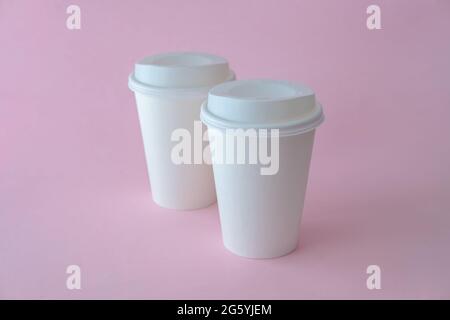 Zwei weiße Pappkaffeetassen auf rosa Hintergrund, Kaffeetasse im Nachbau. Stockfoto