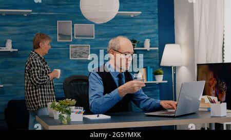 Pensionierter Mann, der online mit Kreditkarte auf einem Laptop bezahlt, der von zu Hause aus arbeitet. Senior Person, die online einkaufen, Rechnungen bezahlen, E-Commerce-Transaktionen mit moderner Technologie über das Internet tätigen Stockfoto
