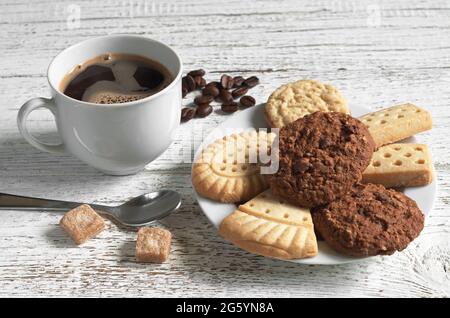 Tasse heißen Kaffee und verschiedene Shortbread-Kekse auf dem Teller auf dem weißen Holztisch Stockfoto