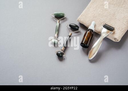 Hautpflegemittel: Mikroneedling Derma Roller, Jade guasha Massagerollen und Serumflasche auf dem grauen Hintergrund Stockfoto