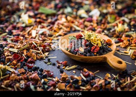 Getrocknete Teeblätter, Früchte und Beeren in Schale auf rustikalem Holztisch Stockfoto