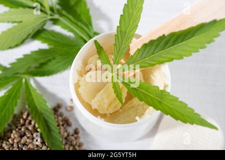 Cannabissamen, junge Hanfblätter und Cannabisbutter auf weißem Hintergrund. Für Kosmetik, Behandlung, Therapie. Nahaufnahme, Draufsicht. Stockfoto