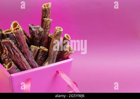 Eine wunderschöne pinke Schachtel mit Leckereien für Haustiere. Getrocknete Zahnartikel für Hunde auf einem rosa Hintergrund. Köstliche Gullet Sticks Mit Rotem Rindfleisch. Rinderösophagus. Stockfoto