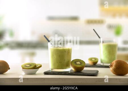 Zwei Gläser Kiwi-Getränk und Behälter mit geschnittenem Obst auf der Küchenbank. Vorderansicht. Stockfoto