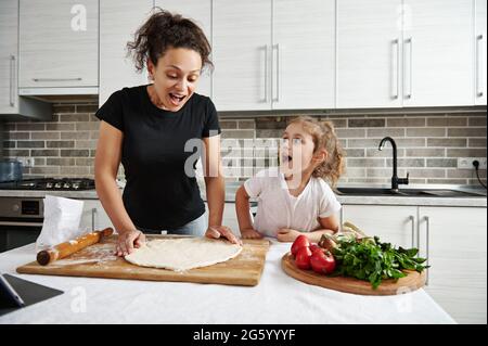 Familienverbringe Zeit Konzept. Kindern beim Kochen beibringen. Glückliche Mutter und Tochter bilden eine runde Form von Pizzateig, kochen zusammen zu Hause. Stockfoto