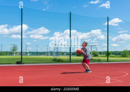 Junge Vorbereitung für Basketball-Schießen auf Playground.Boy führt Schuss bei Basketball-Spiel auf dem Spielplatz während sonnigen Sommertag. Stockfoto