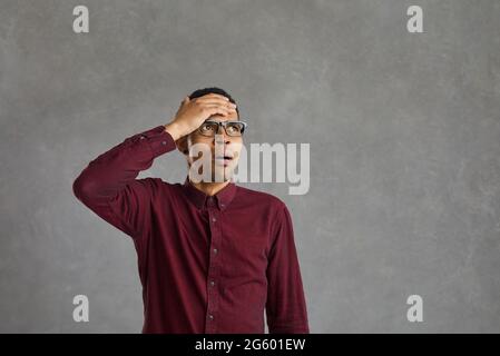 Junger schwarzer Mann, der mit der Hand auf der Stirn aufblickte, fühlte sich schockiert, besorgt und verängstigt Stockfoto