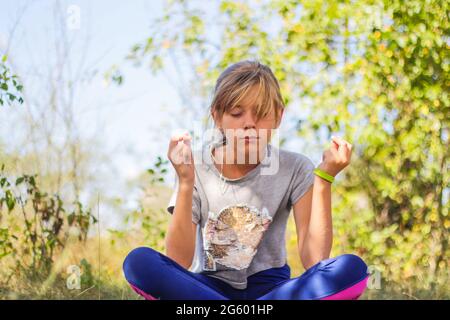 Defocus caucasian preteen Mädchen praktiziert Yoga im Park, Wald, im Freien, draußen. Meditation und Konzentration. Wellness gesunder Lebensstil. Hochformat o Stockfoto