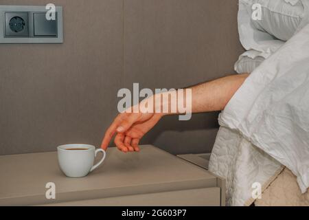 Hand aufs Bett und Suche nach einer Tasse Kaffee zum Aufwachen Stockfoto