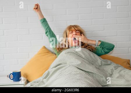 Schlafende Frau, die mit Müdigkeit im Bett gähnt Stockfoto