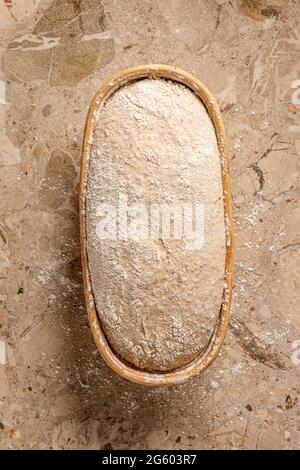 Flache Ansicht von handgefertigtem Sauerteig-Brot auf einer Marmorarbeitsfläche. Teig nach dem Gären in traditionellem Banneton zum Backen bereit Stockfoto